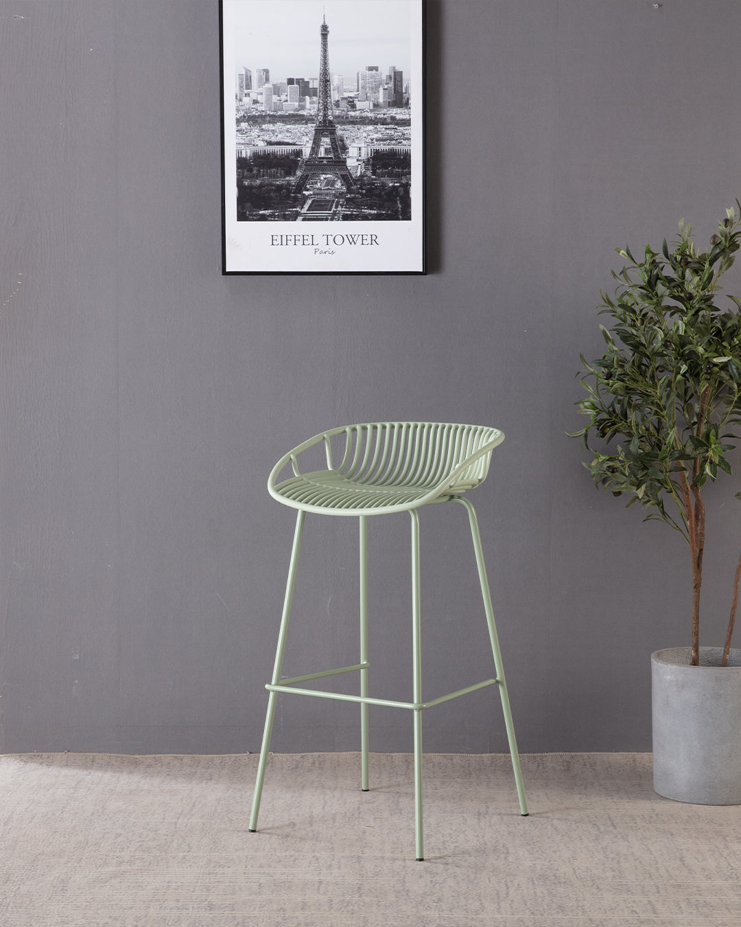 Green bar stool in a room with a gray wall, framed picture, and plant.